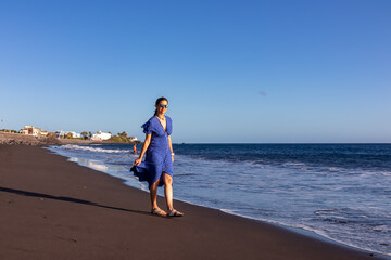 Happy luxury woman in dress walking on the beach Playa Valle Gran Rey seen from Promenade de Playa de La Calera in Valle Gran Rey on La Gomera, Canary Islands, Spain, Europe. Dark volcanic sand beach