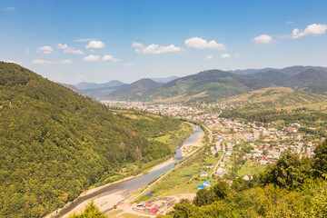Fototapeta na wymiar View from a high mountain to a valley between mountains with a river and a village on a summer day. View over the hills, mountains, valley, river and village. Carpathians. Ukraine