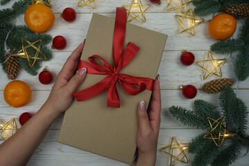 A woman's hand holds a gift in a craft package with a red satin bow 