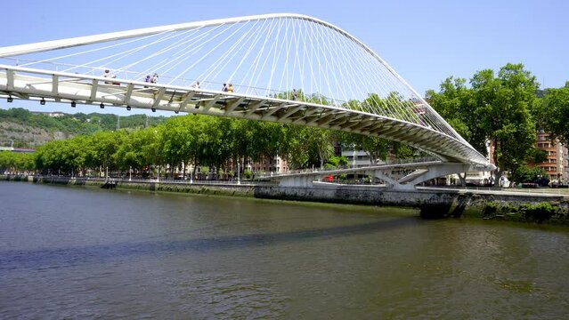 Bilbao, SPAIN - July 19 2022: Zubizuri Bridge, also called the Campo Volantin Bridge. is a tied arch footbridge across the Nervion River in Bilbao, Spain. People passing. Static video 