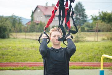 Professional athlete stretches and strengthens his arms, shoulders and pectoral muscles with trx fitness straps. Support training for maximum performance. Focused performance