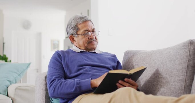 Video Of Happy Senior Biracial Man Relaxing On Couch Reading Book At Home