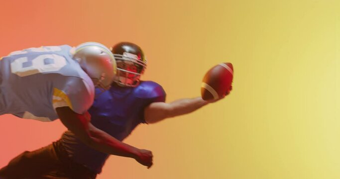 Video of diverse american football players tackling with ball over yellow to orange background