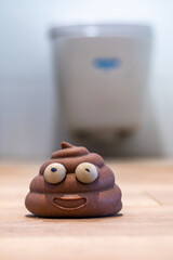 A toy poop laying on a wooden floor by a WC