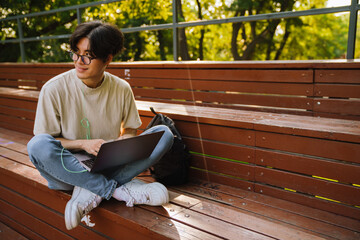 Young smiling asian boy in glasses with laptop looking aside