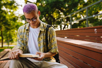 Young handsome stylish smiling boy in glasses reading book
