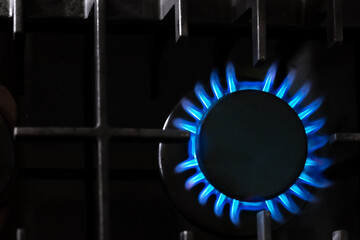 Gas burner with a blue flame on a black kitchen stove, top view, selective soft focus, copy space....