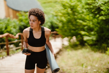 Young woman in sportswear walking with mat after yoga practice