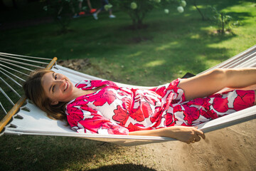 Young blonde woman resting in a comfortable hammock in a green garden on sunny day.