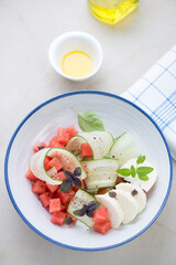 Plate with watermelon, cucumber and goat cheese salad on a beige stone background, vertical shot, elevated view