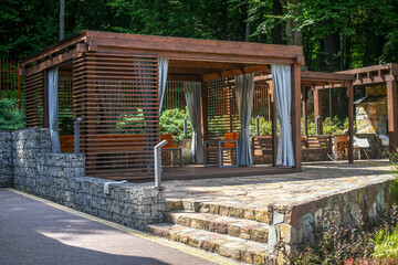 Close up wooden gazebo decorated with gabion elements and natural stone pavement. 