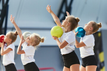 Group of kids, little girls, beginner gymnastics athletes in sports uniform at training at sports gym, indoors. Concept of sport, achievements, studying - obrazy, fototapety, plakaty