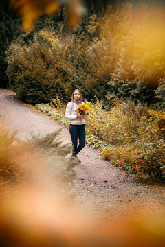 beautiful smiling girl in pink sport jacket walking in autumn park with a bouquet of autumn leaves holding in her hands