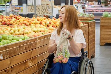 Red-haired woman who uses a wheelchair in a supermarket chooses fruits