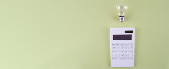 The concept of savings electricity. Reducing the payment of utility bills. A incandescent lamp, calculator on a olive background. Flat lay, top view.
