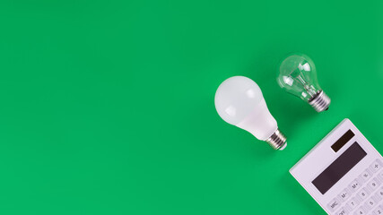 White calculator and incandescent lamp or LED bulb on green background. Concept showing the payment...