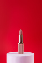 Nude, beige Lipstick on White Podium on red background. Design Template of Fashion Cosmetics Product for Ads, flyer, banner or Magazine Background.