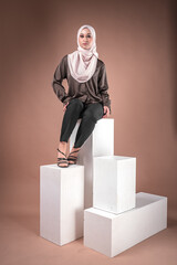 Portrait of a beautiful female model wearing hijab, a lifestyle apparel for Muslim women isolated on brown background. Idul Fitri and hijab fashion concept.