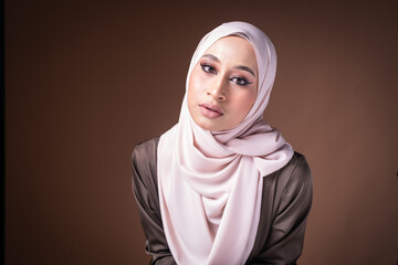 Portrait of a beautiful female model wearing hijab, a lifestyle apparel for Muslim women isolated on brown background. Idul Fitri and hijab fashion concept.