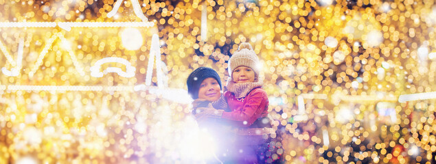 Little cute kids - girl and boy attend the fun fair in the evening at the snow - Christmas market