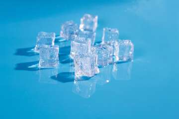 Top above overhead close up macro view photo of ice cubes and water drops on blue background with copy empty blank space.