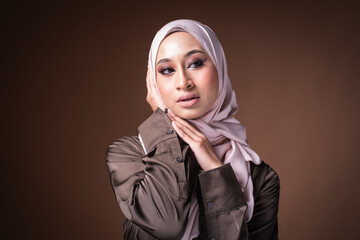 Portrait of a beautiful female model wearing hijab, a lifestyle apparel for Muslim women isolated on brown background. Idul Fitri and hijab fashion concept.