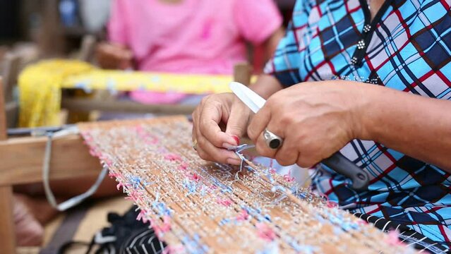 Closeup hands of old female person making Mudmee cloth, a handicraft for woman at home in rural Thailand 