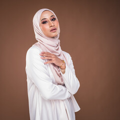 Portrait of a beautiful female model wearing hijab, a lifestyle apparel for Muslim women isolated on brown background. Idul Fitri and hijab fashion concept.