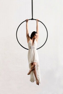 Fit graceful female dancer hanging from aerial hoop in white studio