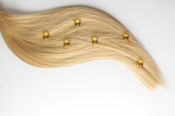 A hair care oil or serum in golden capsules lying on a blond hair strand, product marketing mockup