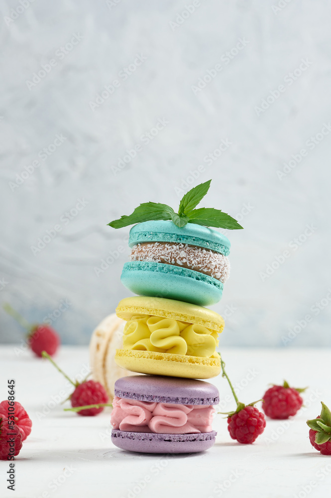 Poster stack of multicolored macaroons and red raspberries on a white background