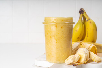Bananas jam in small glass jar with fresh bananas on  white table background 