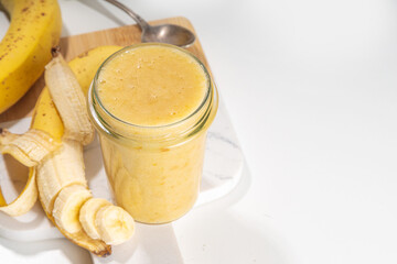 Bananas jam in small glass jar with fresh bananas on  white table background 