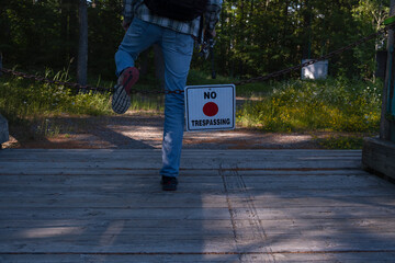 Man stepping over a chain with hanging sign no trespassing.