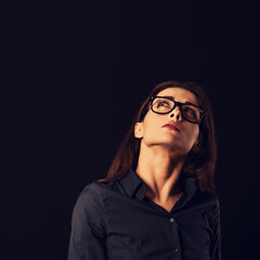 Cute thinking serious business woman looking up and scratching her head and deciding riddle in blue shirt on black background with empty copy space for text. Closeup
