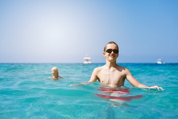 Child boy with swimming goggles swims in the sea next to a rock during a happy summer vacation in Corfu, Greece
