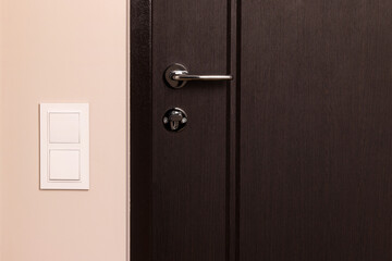 White electrical switch on beige wall next to the wooden door in modern apartment