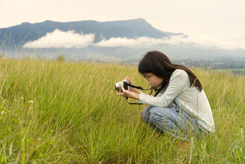 An Asian kid is sitting and taking pictures from her digital camera with mountains and clouds in the background from Thailand.