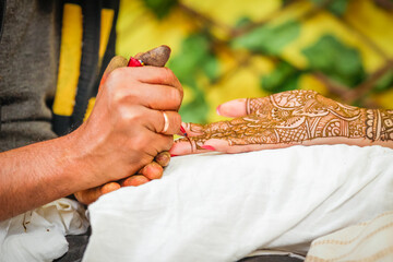 Mehndi artist painting henna on woman's hand.