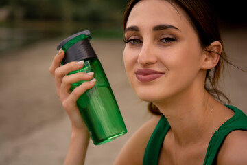 a girl in a sports uniform holds a bottle in her hand, a girl drinks water from a bottle, a girl is dressed in a green tracksuit top and cycling shorts, water balance, outdoor sports, sports lifestyle