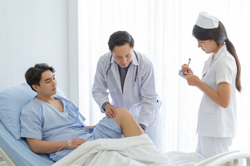 Obraz premium Senior doctor and young male patient who lie on the bed while checking symptom, consult and explain with nurse taking note and supporting in hospital wards.