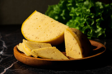 Large chunks and slices of cheese with walnuts on a wooden plate on a dark marble background