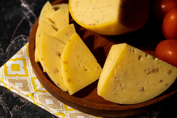 Large chunks and slices of cheese with walnuts on a wooden plate on a dark marble background