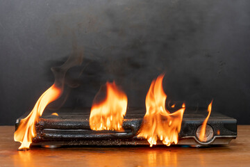 Obraz premium A DVD player is burning on the table, flames are rising up, the case has melted, a fire has started in the apartment.