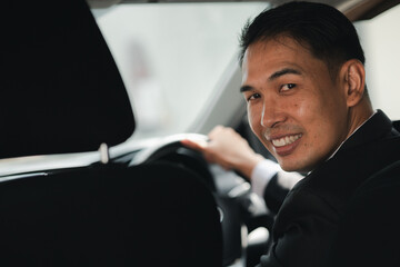Close-up photo of an Asian man in a formal suit sitting in a car, traveling by car, safe driving, respecting traffic rules.