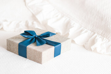 Holiday present and luxury online shopping delivery, wrapped linen gift box with blue ribbon on bed...