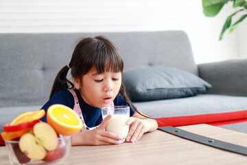 Cute little Asian girl drinking milk. Children are forced to drink milk. Concept of healthy food...
