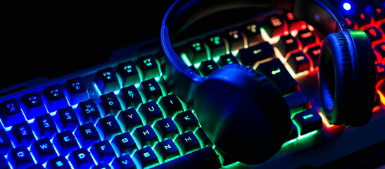 Pro gaming illuminated desk, headset, keyboard, computer neon lights. Cyber sport equipment laying on desktop, ready for online video gaming.Dark shot.Banner,advertisement. © ARVD73