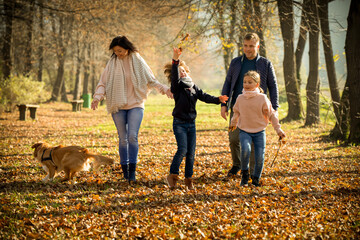 Naklejka na ściany i meble Happy family with dog walking in the autumn park among yellow leaves