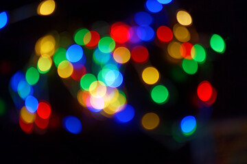 Defocused bokeh lights on black background, an abstract naturally blurred backdrop for Christmas eve or birthday party. Festive light texture. Colorful garland in blur. Overlay effect for design. 2023